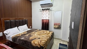 A bedroom with a bed, a ceiling fan, an air conditioning unit, a window with curtains, and a mirror. - Om Home Stay (Agra)