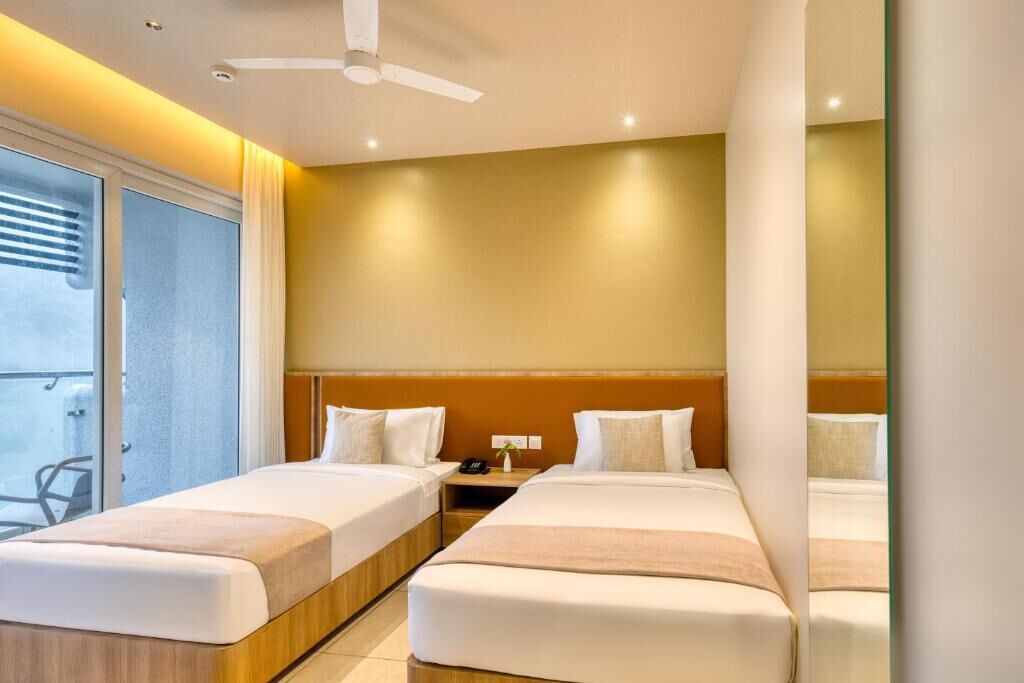 Habitación de hotel con dos camas, ventilador de techo, mesita de noche y vistas al exterior.