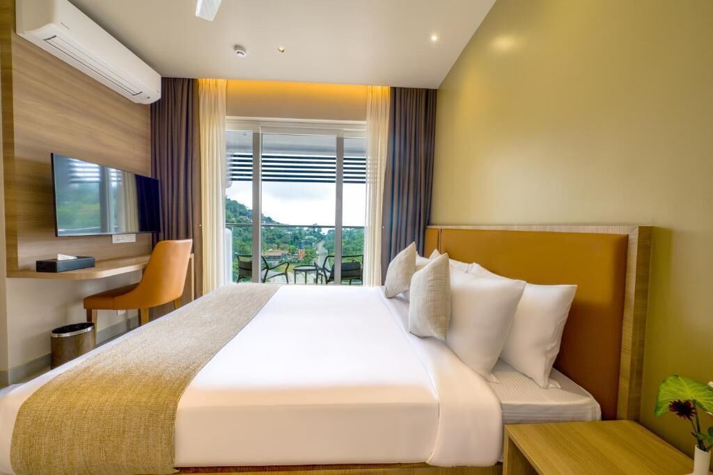 Une chambre d’hôtel avec un grand lit, un bureau avec une chaise, une télévision et un balcon donnant sur l’extérieur.