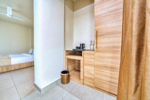 Una habitación pequeña y moderna con una cama, un armario de madera, un bote de basura y un ventilador de techo.
