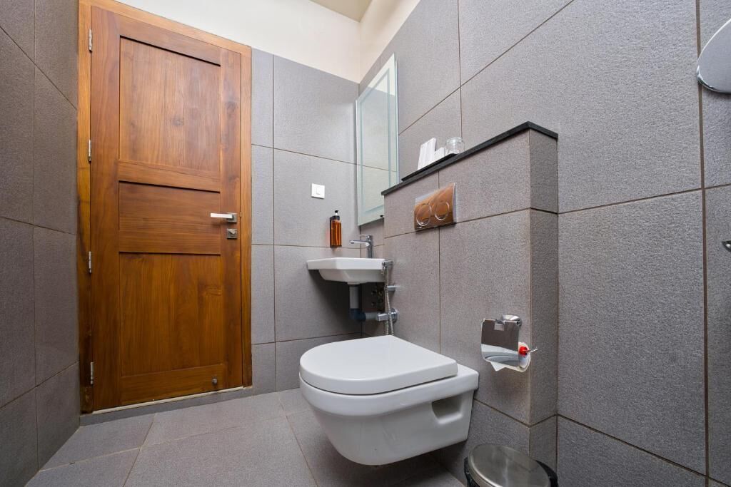 A bathroom with a wooden door, a white toilet, a sink, and a mirror.