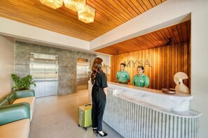 Zona de recepción con techo de madera, mostrador de mármol y pared verde.