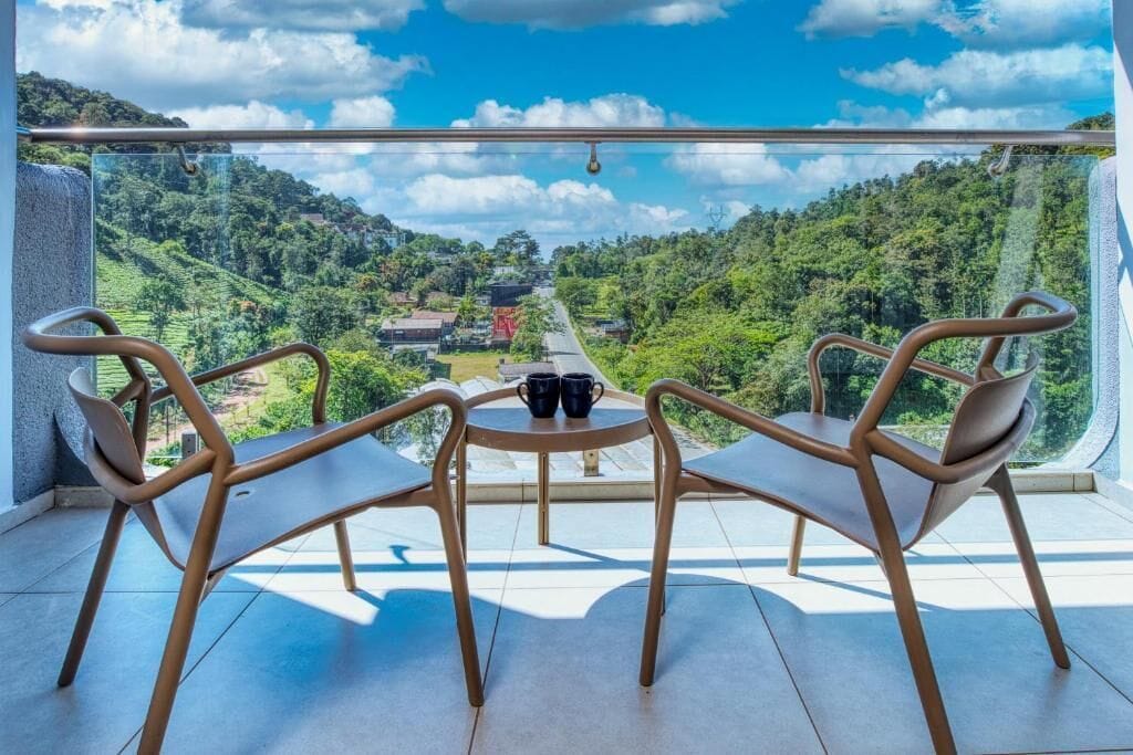 Un balcón con dos sillas y una mesa, con vistas a un paisaje verde exuberante y un cielo despejado.