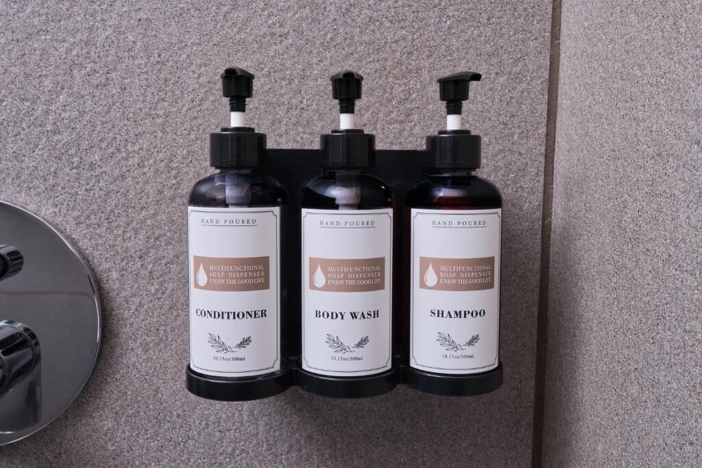 Three hand-poured bottles of conditioner, body wash, and shampoo on a wall-mounted dispenser.