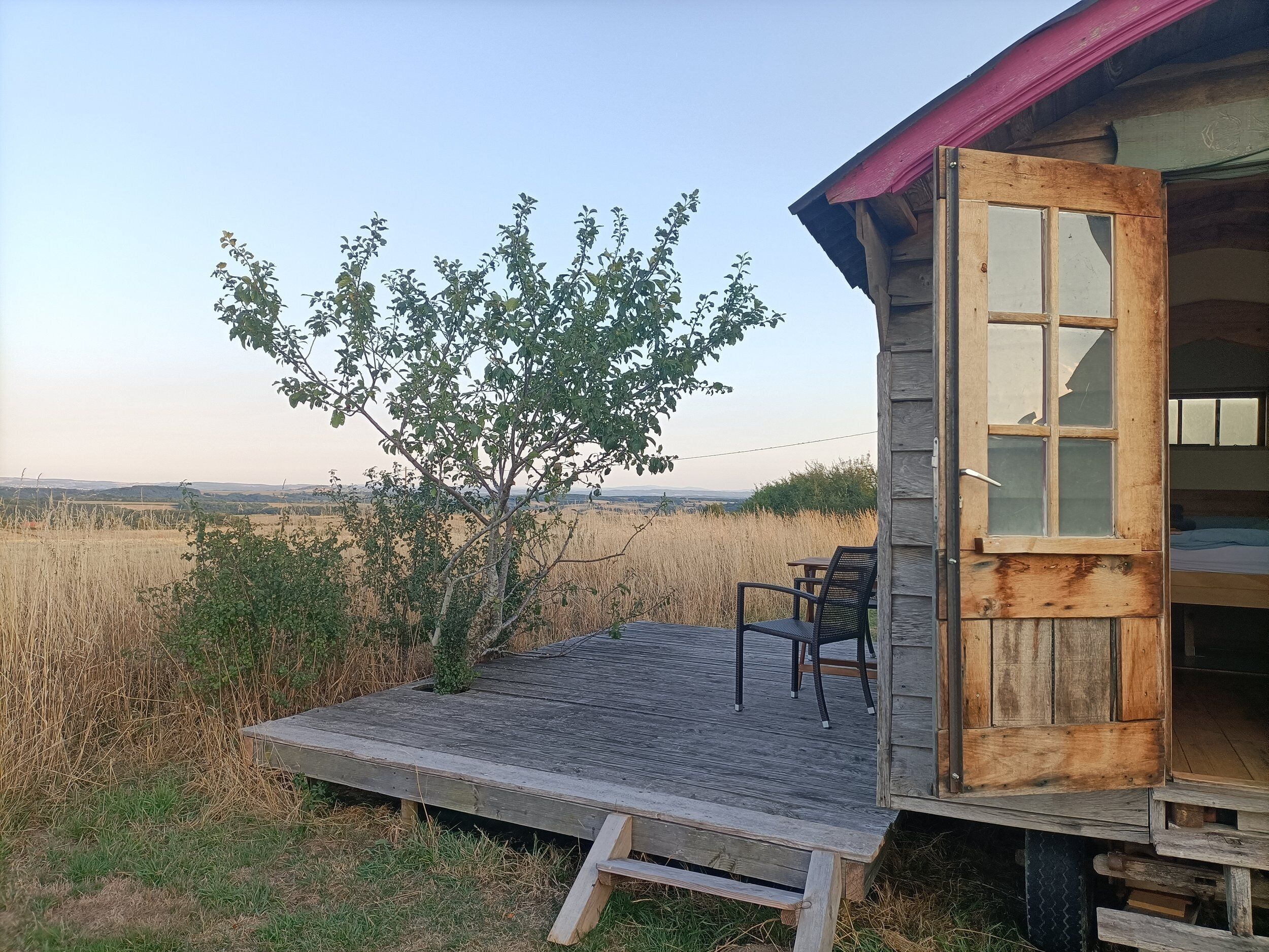 Una cabaña de madera con un porche, un árbol y vistas del paisaje.