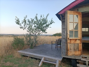 A wooden cabin with a deck, a tree, and a view of the landscape.