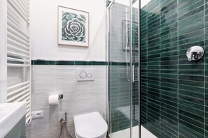 Ein Badezimmer mit Duschkabine aus Glas, Toilette, Handtuchhalter und einem gerahmten Bild an der Wand.