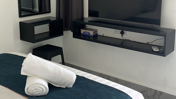 A hotel room with a bed, a television, a mirror, and a wall-mounted air conditioning unit.