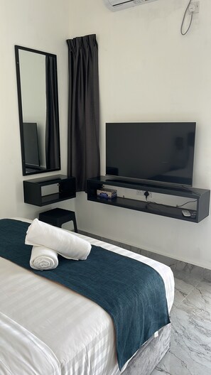 A hotel room with a bed, a television, a mirror, and a wall-mounted air conditioning unit.