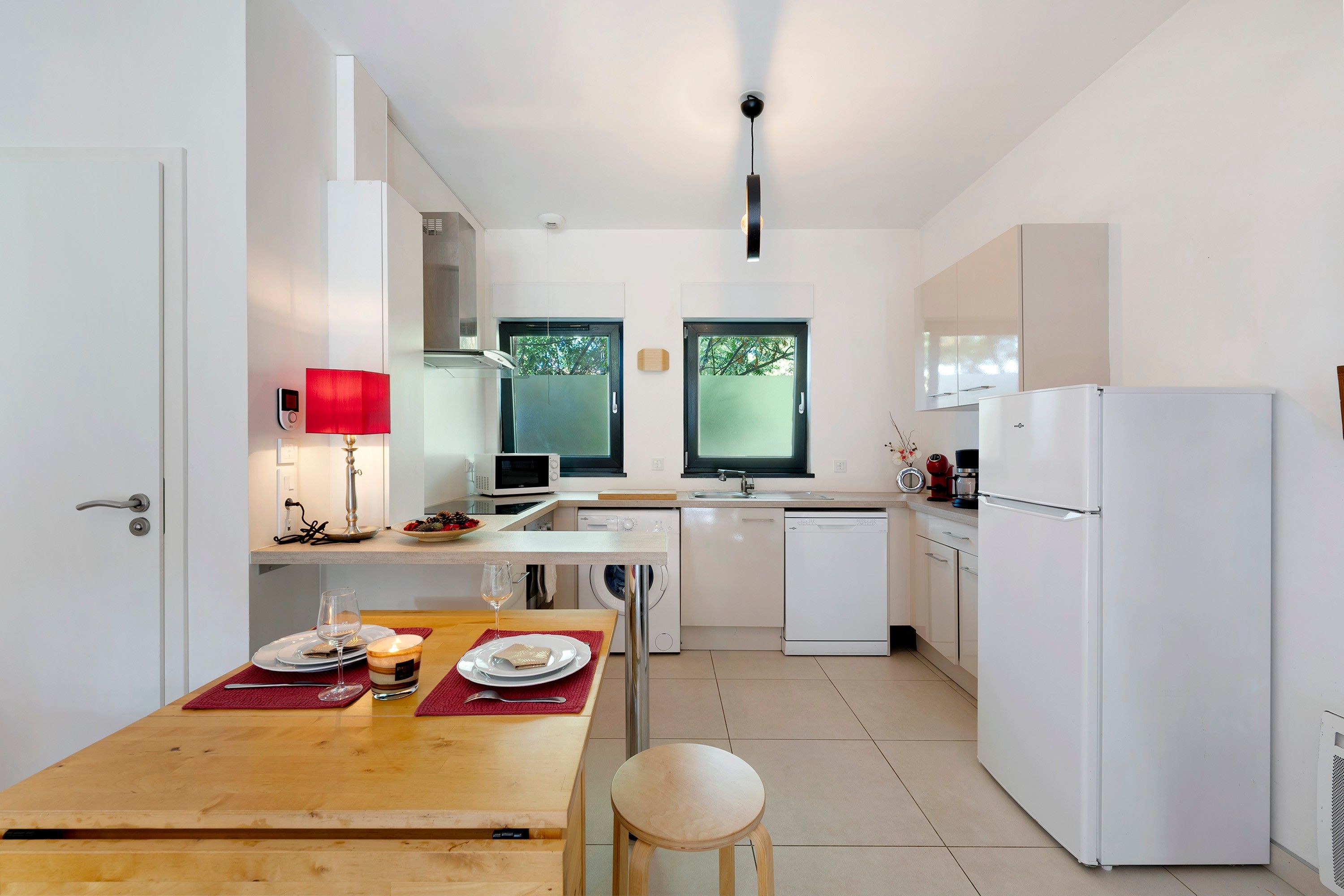 Una cucina moderna con elettrodomestici bianchi, un tavolo da pranzo con piatti e un bicchiere di vino, e una finestra vista alberi.