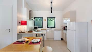 Een moderne keuken met witte apparaten, een eettafel met borden en een wijnglas, en een raam met uitzicht op bomen.