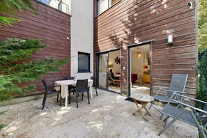 A patio area with a table and chairs, a wooden fence, and a view into the interior of a building.
