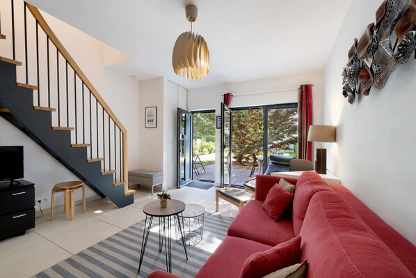 A modern living room with a staircase, a red sofa, a small round table, and a television.