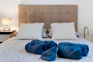 A neatly made bed with two pillows, a bedside lamp, and a glass table with a metal base.