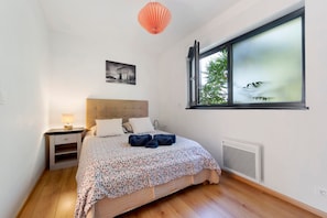 A bedroom with a bed, a nightstand, a window, and a radiator.
