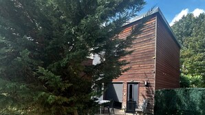 Un edificio moderno con fachada de ladrillo, un porche cubierto con mesas al aire libre y un gran árbol perenne al frente.