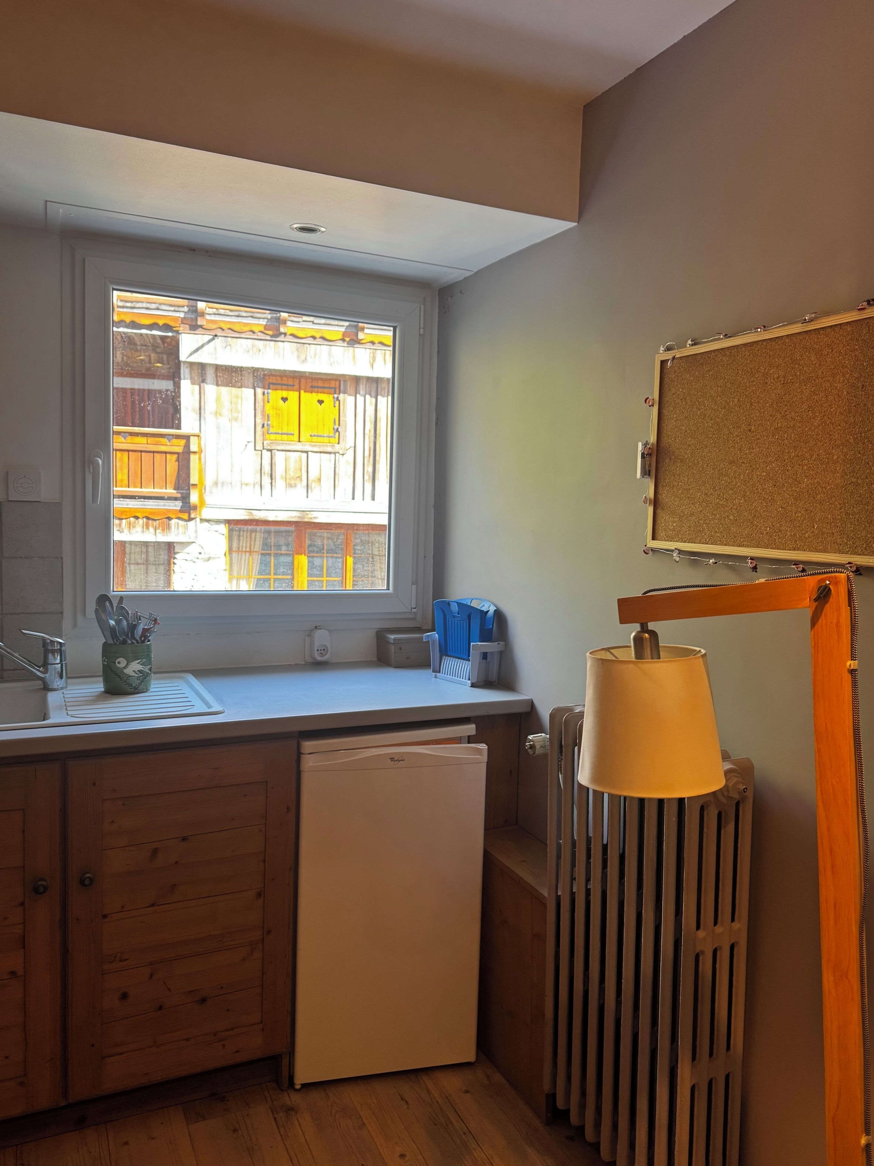 A compact kitchen with a window, a radiator, and a small refrigerator.