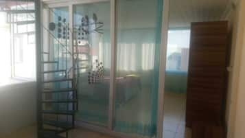 A room with a sliding glass door leading to a balcony, a metal spiral staircase, and a bed with a blue bedspread.