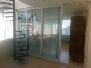 A room with a sliding glass door leading to a balcony, a metal spiral staircase, and a bed with a blue bedspread.