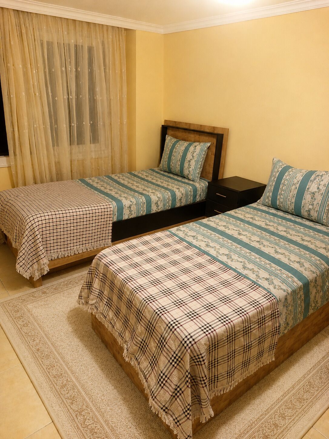 A bedroom with two beds, a nightstand, and a window with curtains.