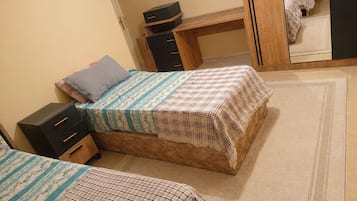 Quarto com duas camas, uma escrivaninha e um guarda-roupa.