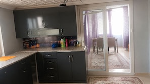 A kitchen with dark cabinets, a countertop, and a dining area with a table and chairs.