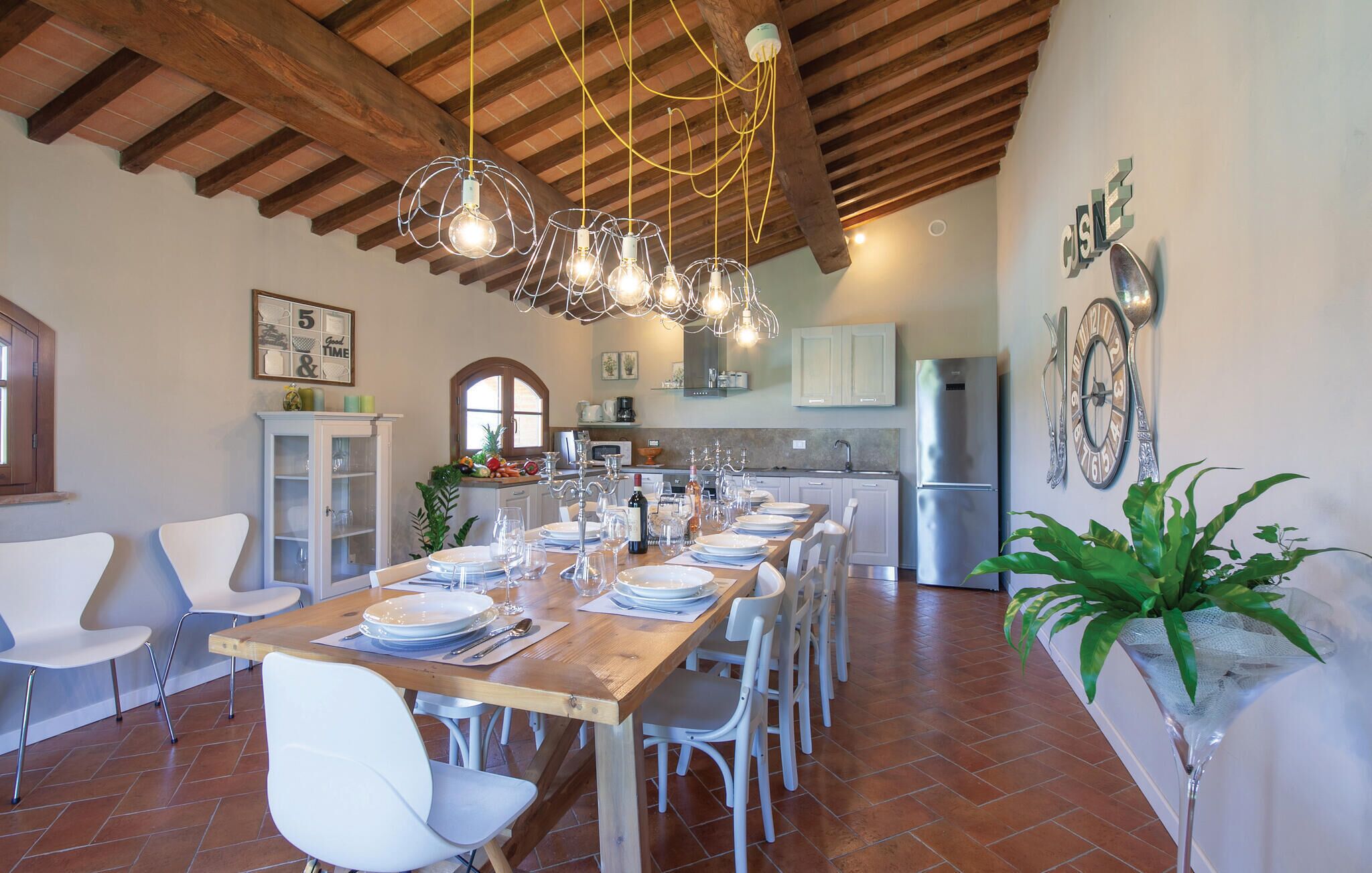 A dining area with a long wooden table set for a meal, surrounded by white chairs.