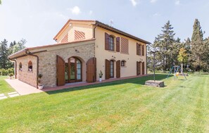 A two-story stone building with a flat roof, arched doorways, and a small garden area with a swing set. - Nice home in Lajatico with private swimming pool, can be inside or outside (Lajatico)