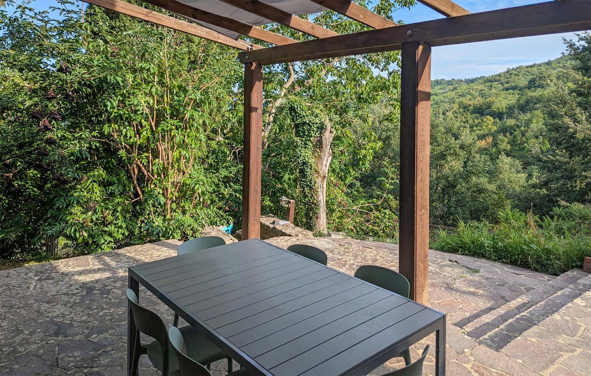 Un patio al aire libre con una mesa y sillas, rodeado de suelo de piedra y una pérgola de madera.