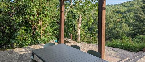 Un patio al aire libre con una mesa y sillas, rodeado de suelo de piedra y una pérgola de madera.