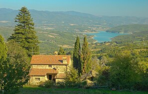 A stone house with a tiled roof surrounded by trees and a view of a lake and mountains in the distance. - Nice home in Caprese Michelangelo (Caprese Michelangelo)