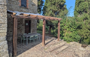 Ein Steinhaus mit einer Holzpergola, einem Tisch und Stühlen vor der Fassade.