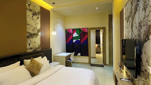Habitación de hotel moderna con una cama grande, un escritorio, un televisor y un baño visible a través de una puerta de vidrio.