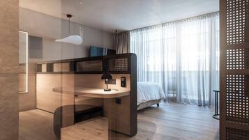 A modern bedroom with a wooden desk, a bed with white bedding, a hanging light fixture, and sheer curtains.