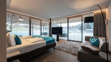 Habitación de hotel moderna con una cama grande, un sofá, un televisor y vistas a un paisaje nevado.