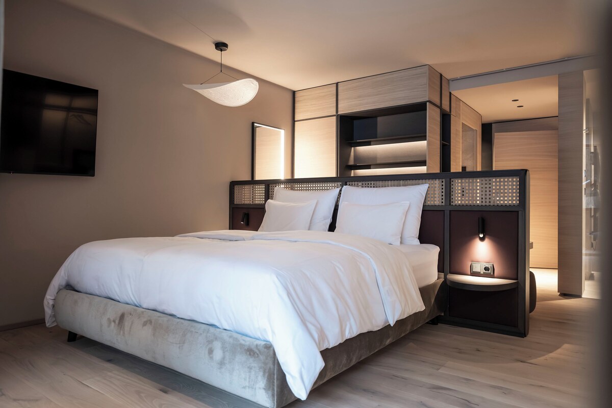A modern bedroom with a large bed, built-in shelving, a flat-screen TV, and ambient lighting.