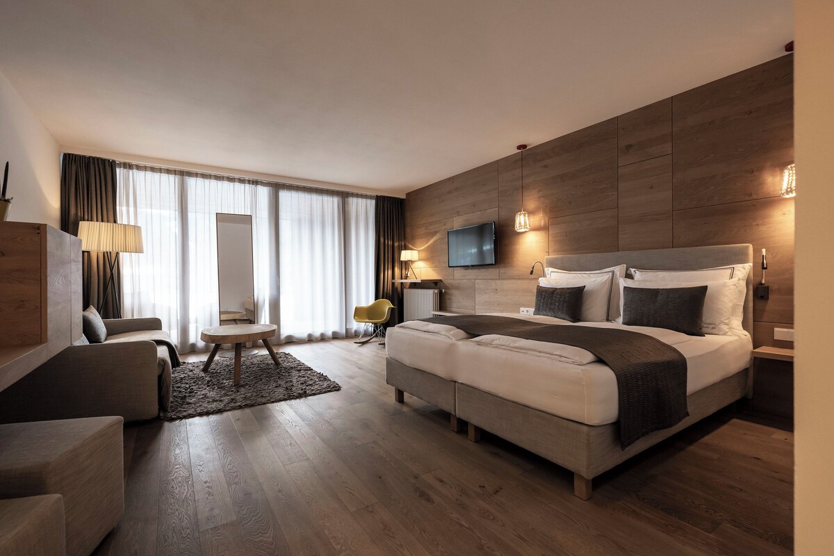 A modern hotel room with a large bed, a sofa, a small table, and a TV.