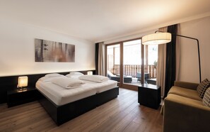 Habitación de hotel con cama, mesita de noche, lámpara, un cuadro, un balcón con mesa y un sofá.