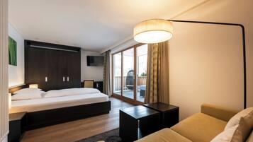 A modern hotel room with a bed, a sofa, a small table, and a large window.