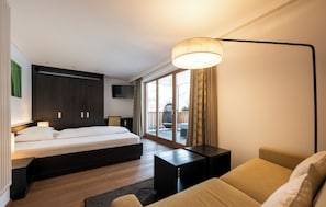 A modern hotel room with a bed, a sofa, a small table, and a large window.