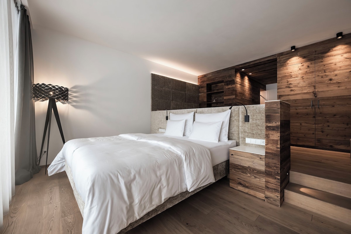 A modern bedroom with a large bed, a floor lamp, and wooden paneling on the walls.