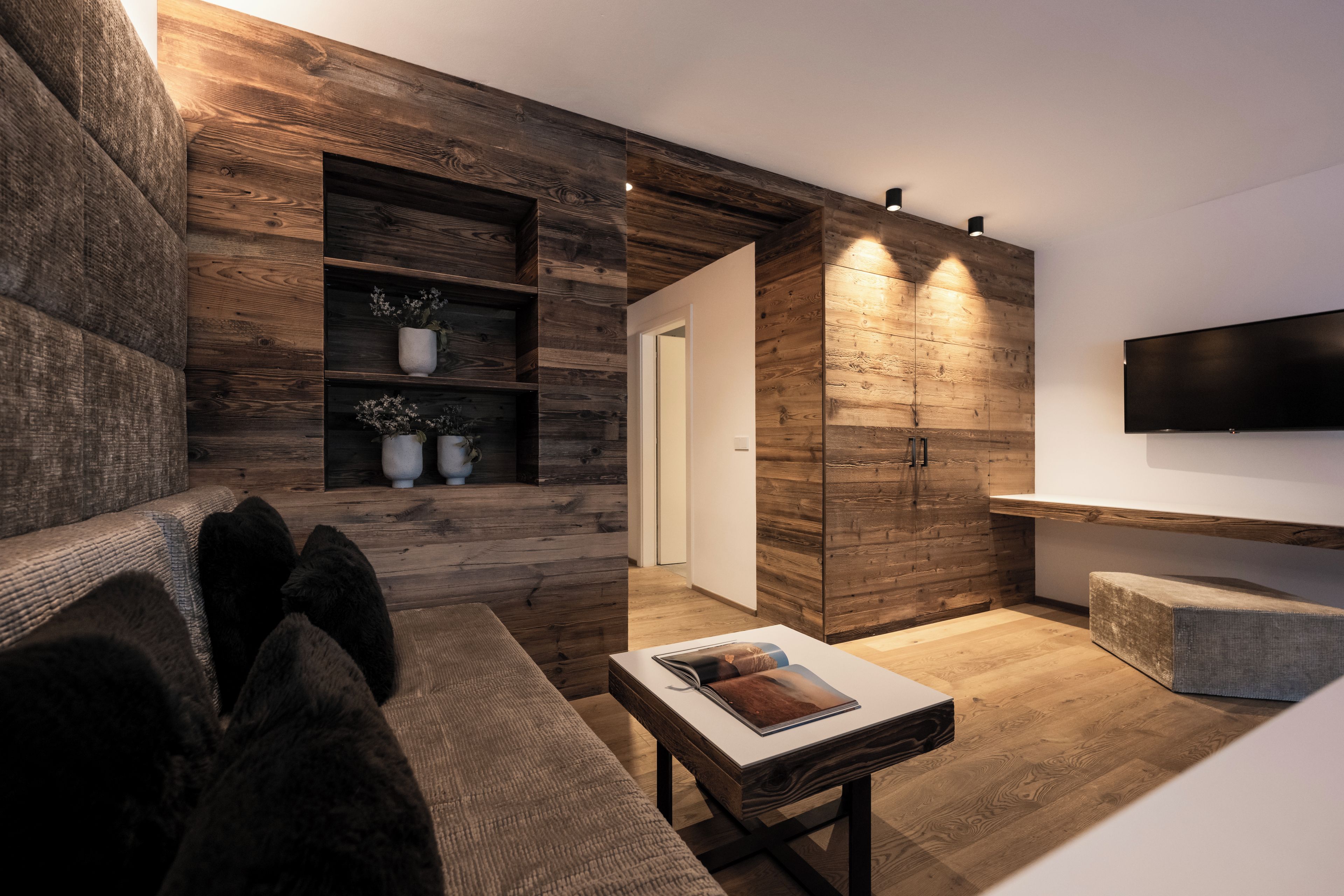 Una sala de estar moderna con una pared decorada en madera, un televisor de pantalla plana montado y un rincón de descanso acogedor con un sofá y una mesita de centro.