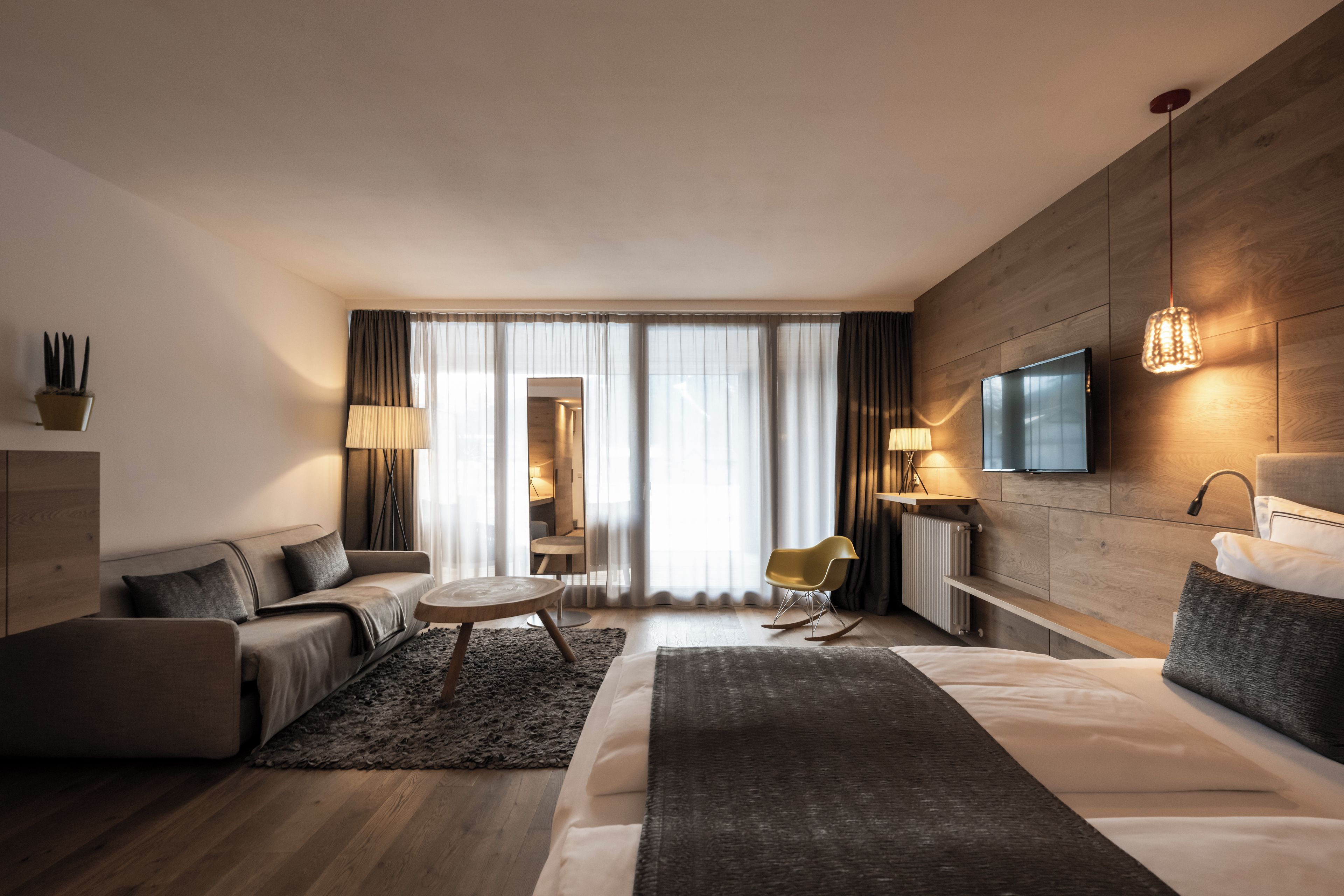 Una habitación de hotel moderna con una cama grande, un sofá, una mesita y un televisor, con vistas a la ciudad desde la ventana.