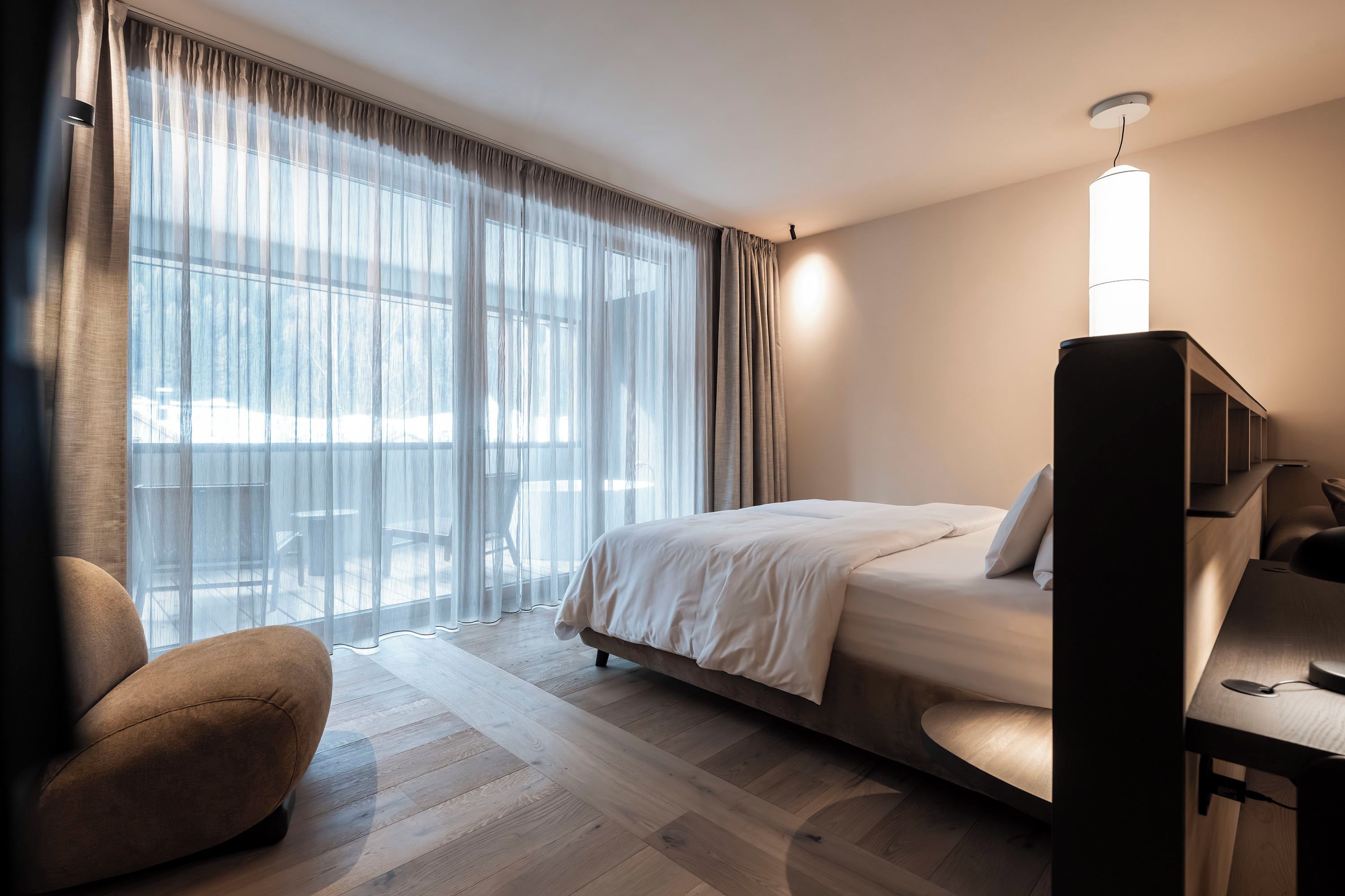 Una habitación de hotel con cama, escritorio, silla y un ventanal con cortinas.