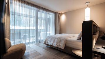 Una habitación de hotel con cama, escritorio, silla y un ventanal con cortinas.