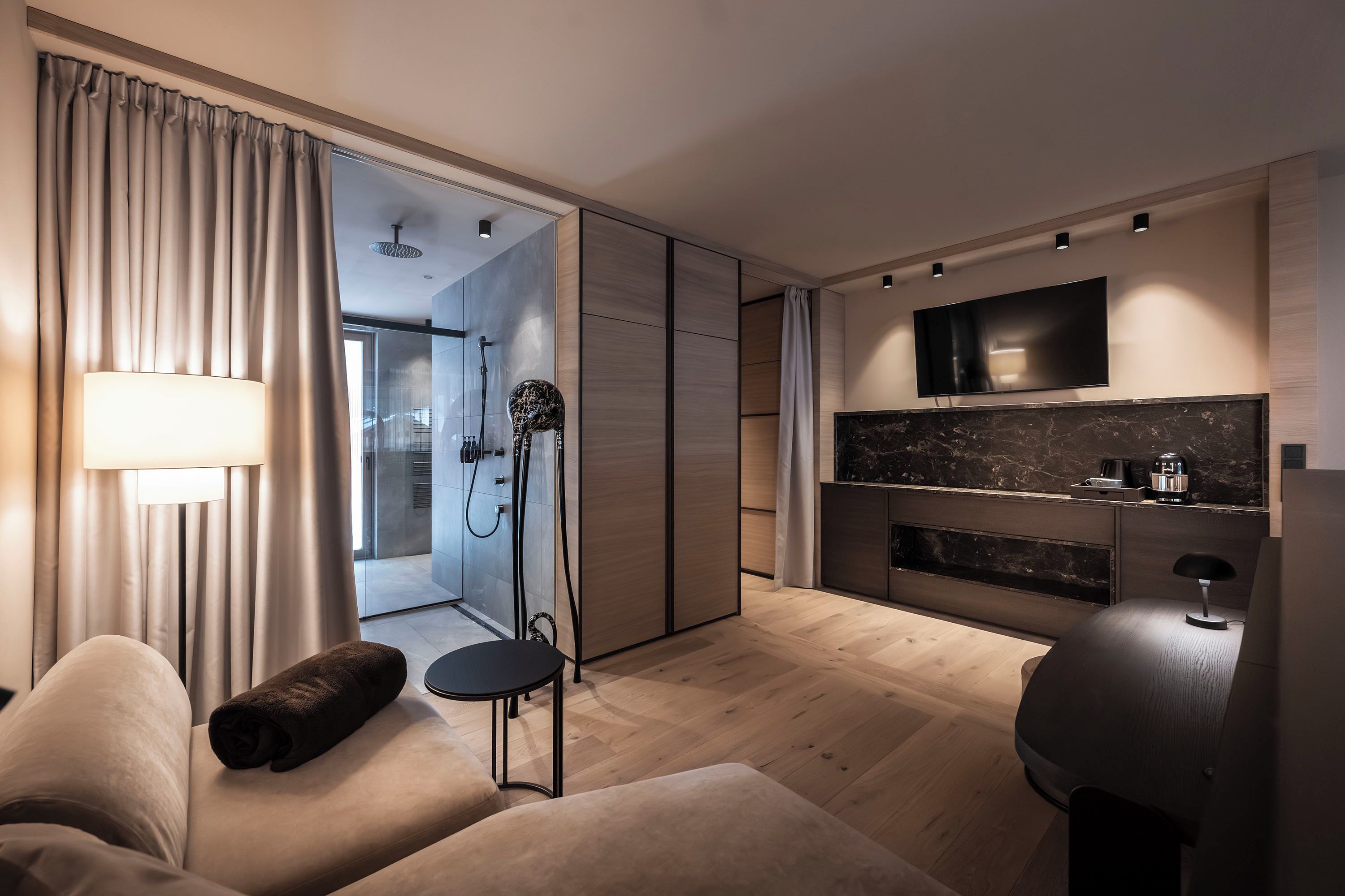 A modern living room with a sofa, a coffee table, a TV mounted on the wall, and a sliding door leading to a bathroom.