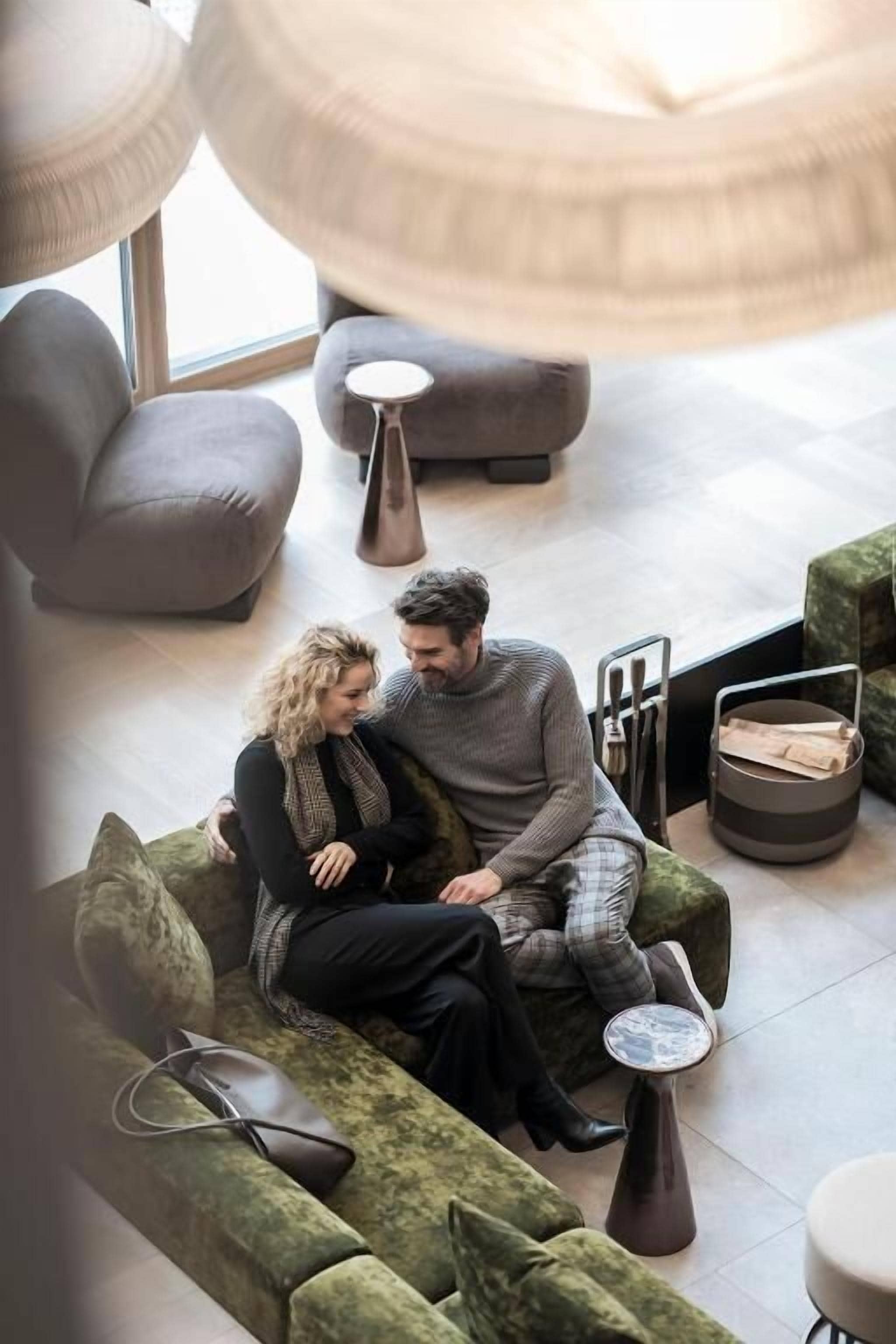 A couple sitting on a green sofa in a modern lounge area with a round table and a small stool.