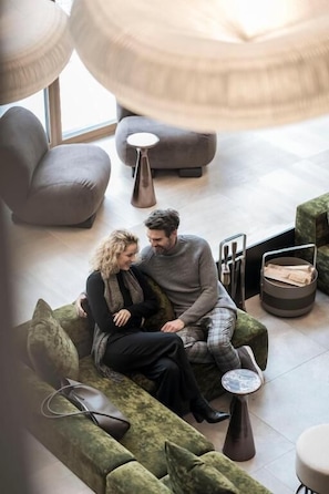 A couple sitting on a green sofa in a modern lounge area with a round table and a small stool. - Hotel Monika - Adults Only (Sesto)