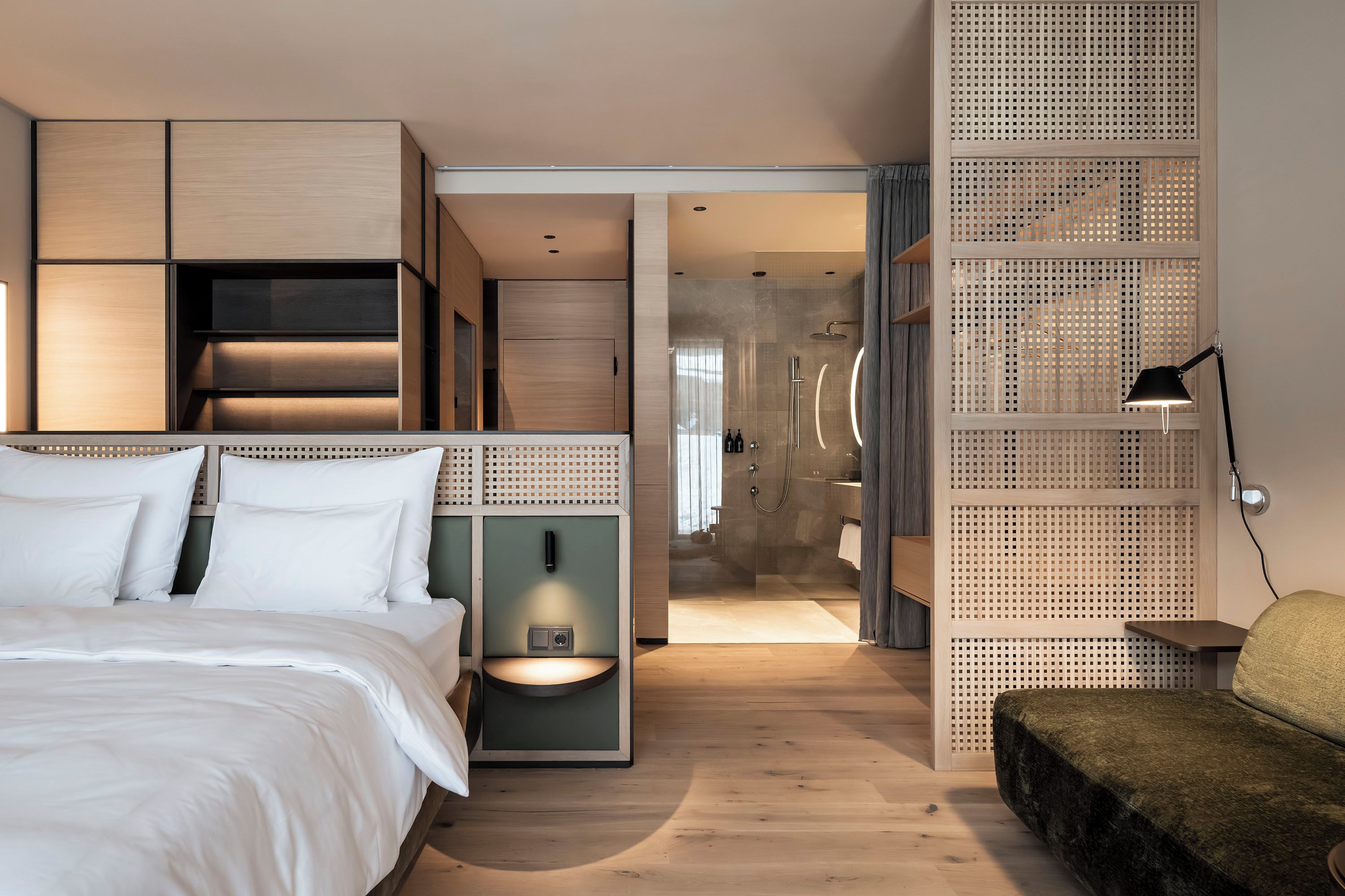 A modern hotel room with a bed, a desk, a shower area, and a seating area.