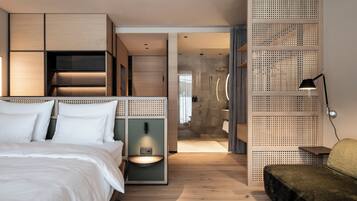 A modern hotel room with a bed, a desk, a shower area, and a seating area.